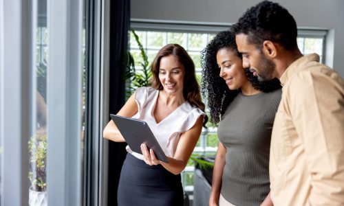Happy real estate agent showing a couple some pictures using a digital tablet while looking at a house for sale